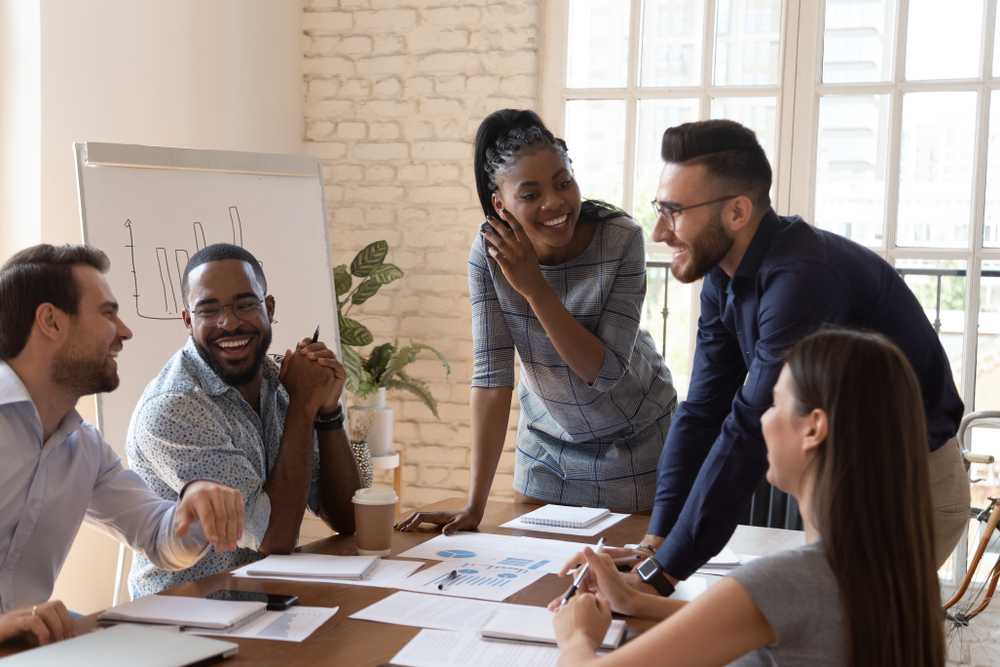Five people gathered around a meeting table showing high employee engagement.