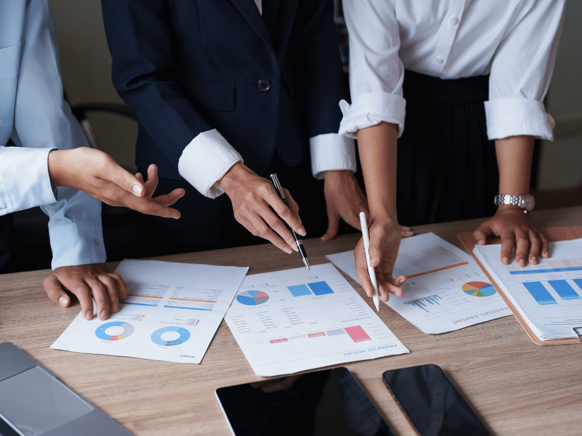 The torsos and arms of three accountants as they look at sheets of AI generated statistics wandering how this will affect recruitment.