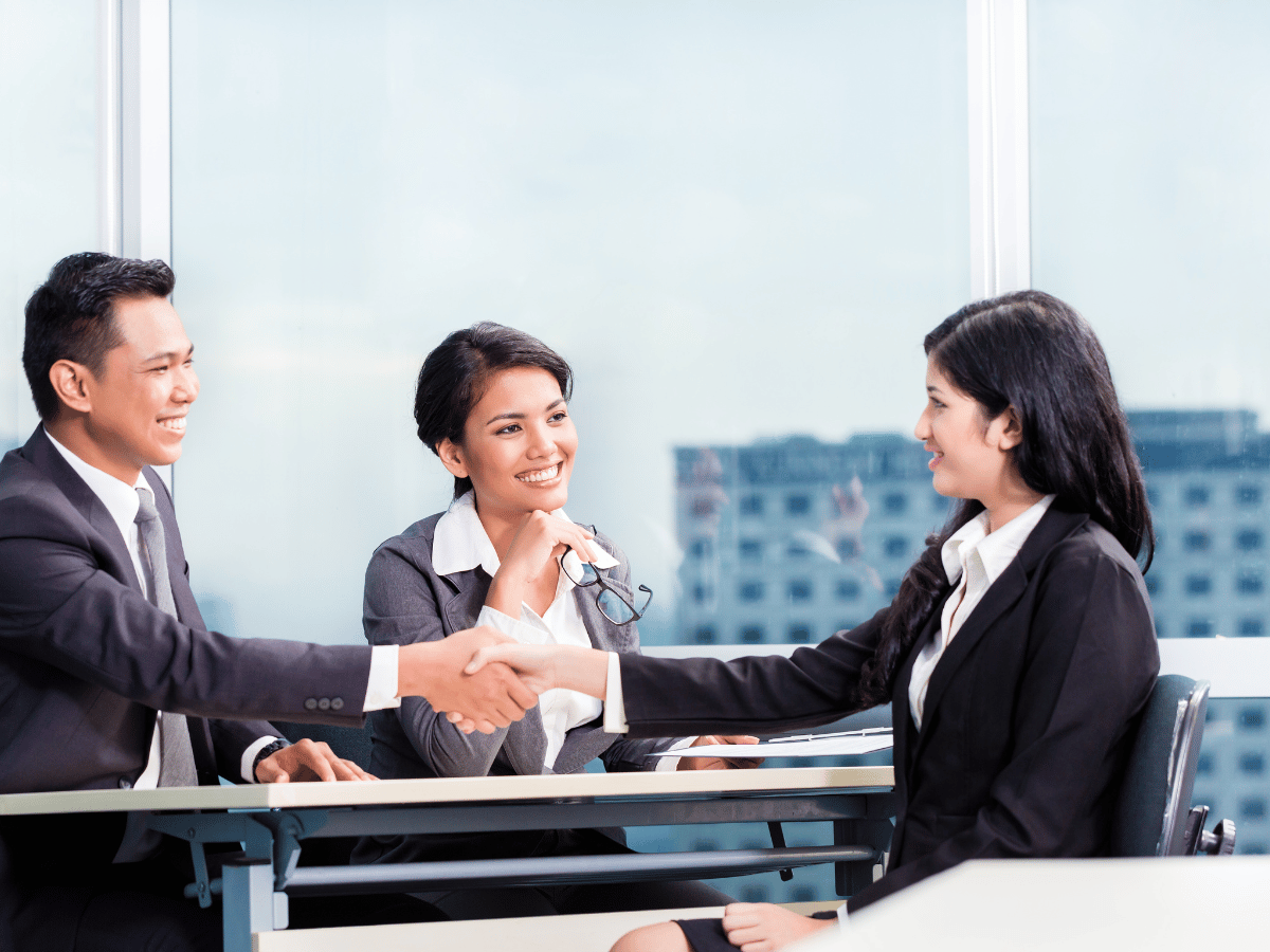 A smartly dressed male and female interviewer shake hands with a successful female candidate after getting recruited.