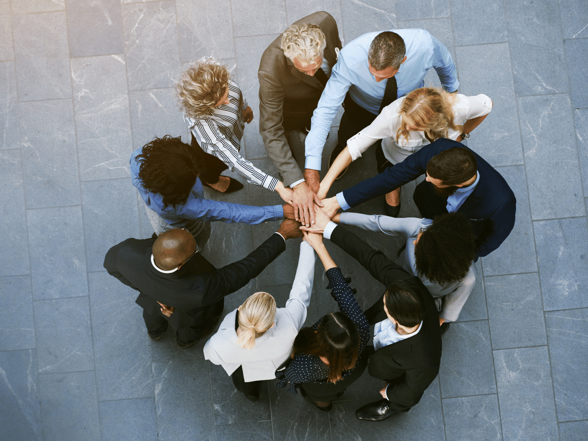 overhead shot of several people in business dress standing in a circle eith one arm outstretched and meeting in the middle.